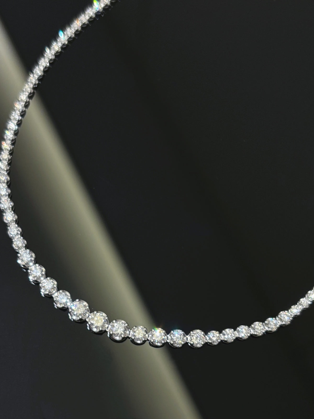Graduated round diamond tennis necklace in white metal, close-up of the larger front diamonds
