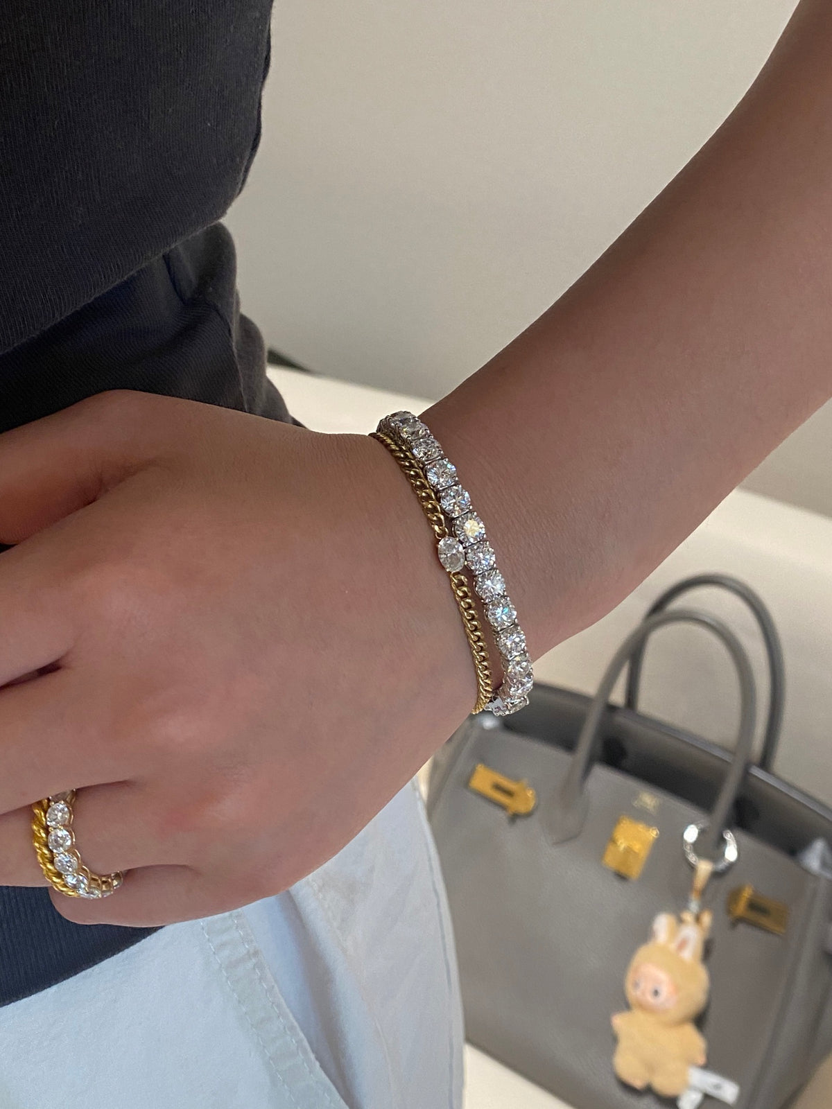 Original wearing view of the larger white-metal round diamond tennis bracelet; separate gold chain bracelet and ring are styling accessories