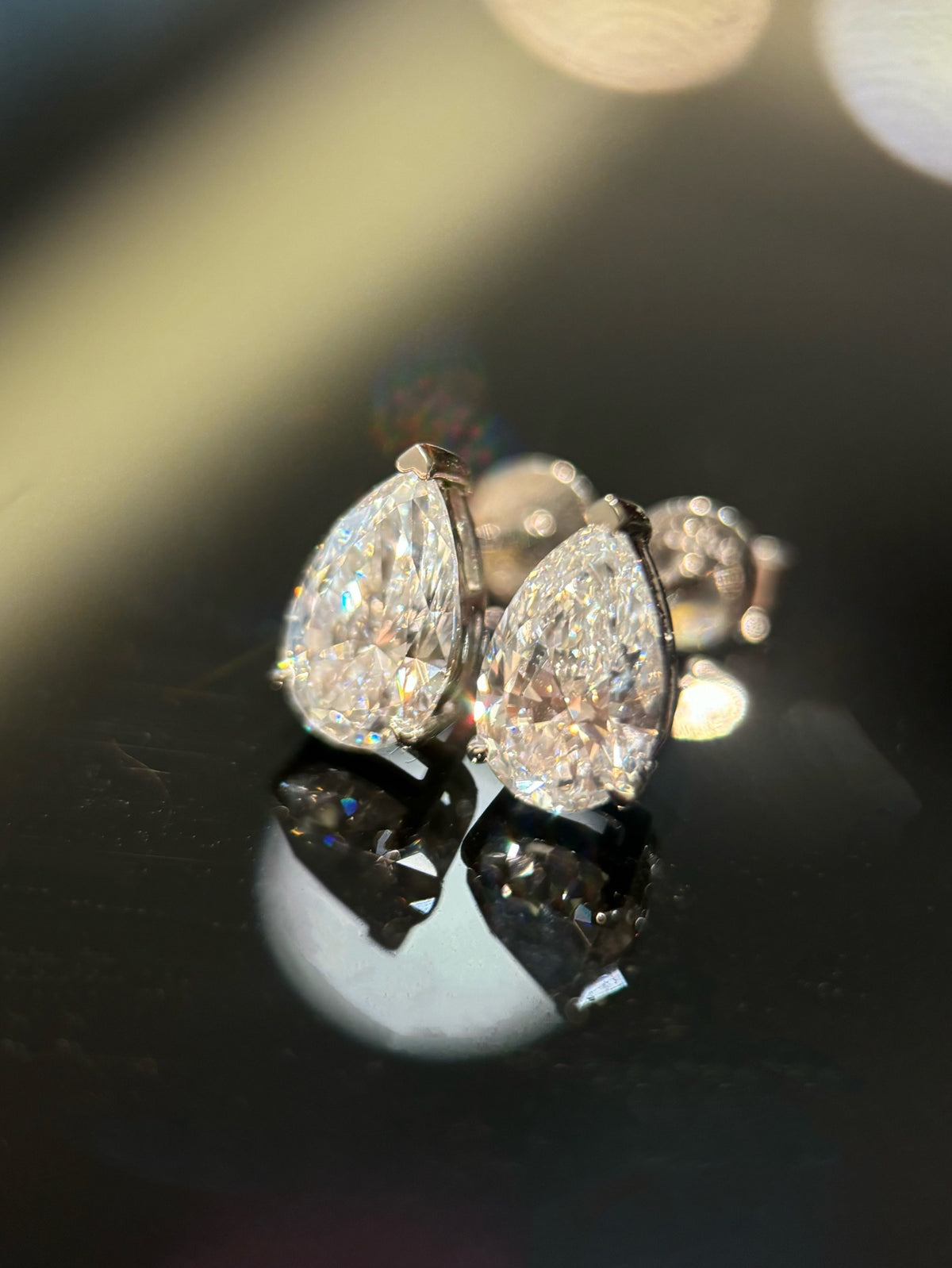 Pear-cut diamond stud earrings in white gold, original angled view with butterfly backs