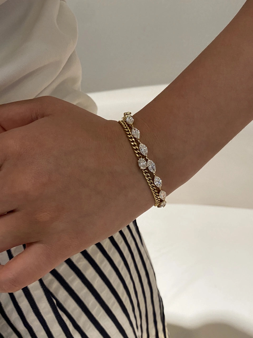 A chain bracelet and a clear-stone bracelet worn together on a wrist.