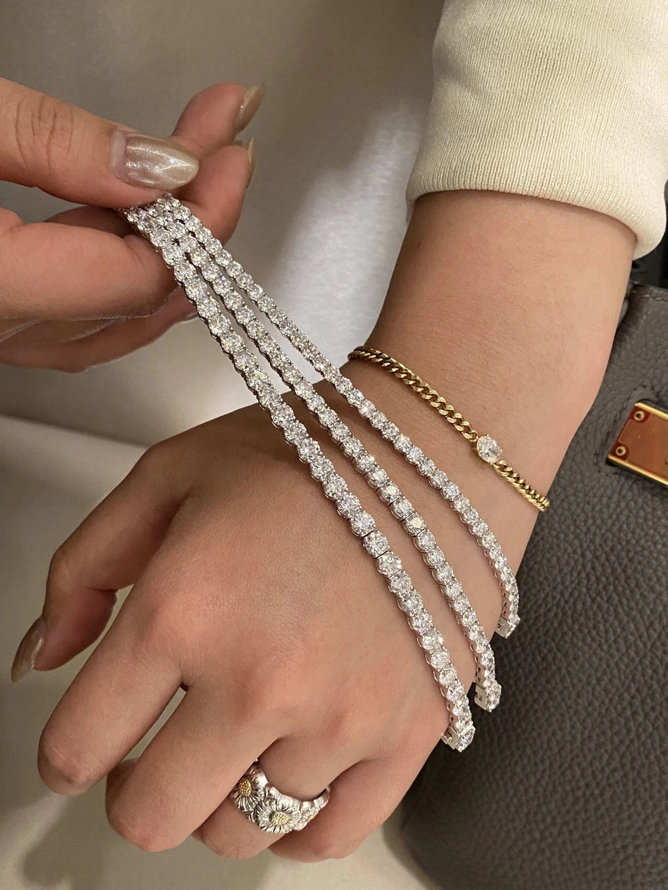A hand holding several strands of clear-stone jewelry over a wrist.