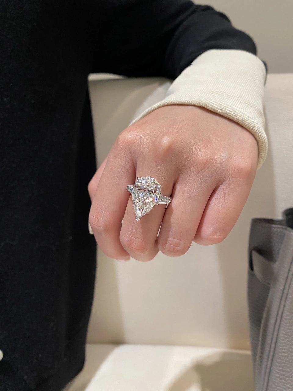 A pear-shaped clear-stone ring with side stones worn on a hand.