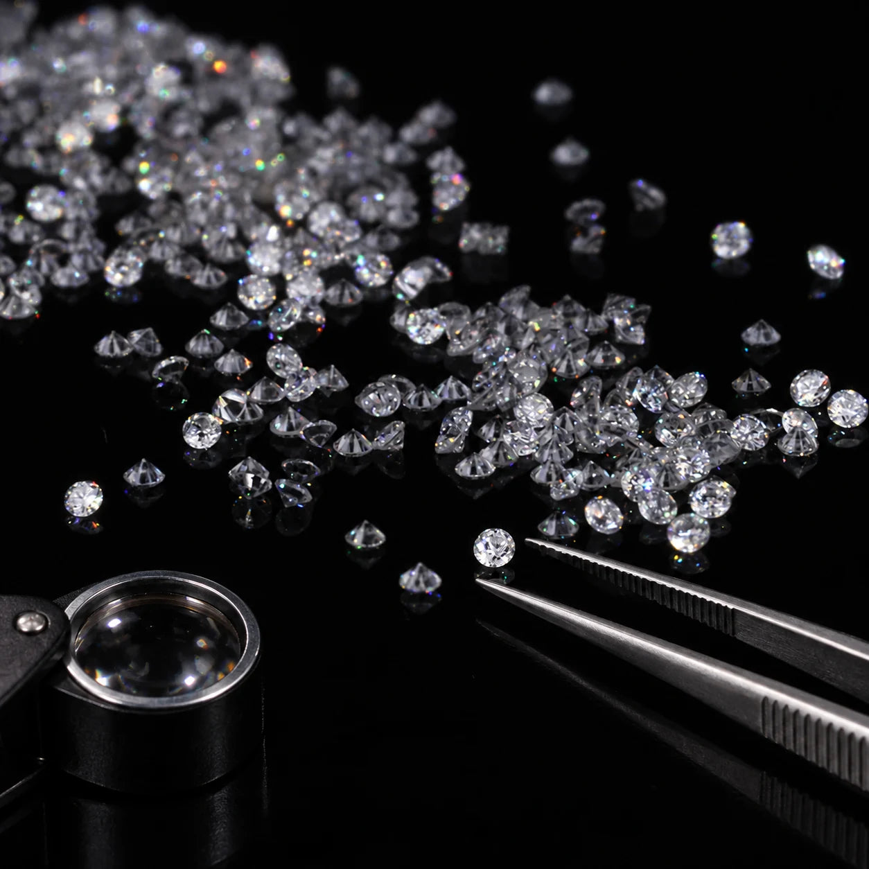 Loose diamonds with jeweler’s tweezers and a loupe on a black surface.