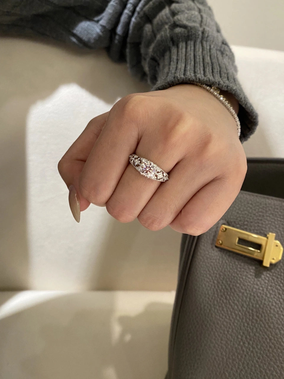 A clear-stone band worn on a hand beneath a gray knitted sleeve.