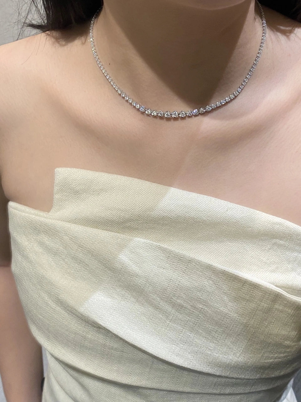 A single-row clear-stone necklace worn above a white folded neckline.